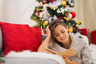 Woman reading book near Christmas tree