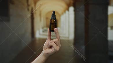 Man holding medicine bottle in historic university hallway with arched ceiling indoors highlighting education and health imagery