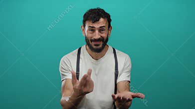 Hispanic man with beard gesturing for begging against a green background, wearing a white shirt and suspenders, expressing emotion