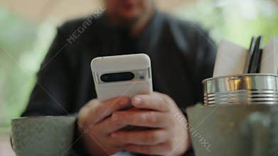 Person Using Smartphone at Cafe Table with Coffee and Utensils