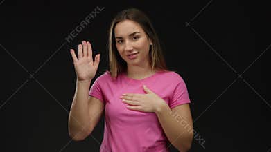 Young blonde woman in pink shirt taking an oath against an isolated black background in a gesture of sincerity and commitment