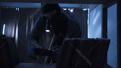 Thief in black balaclava with flashlight making housebreak. Robber criminal entering a house for money stealing at night