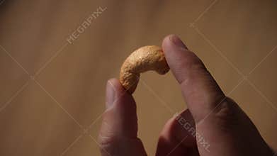 Close-up of hand holding single raw cashew nut