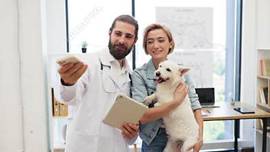 Veterinarian and pet owner taking selfie with dog during checkup