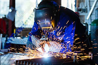 Welder welding metal in workshop with sparks