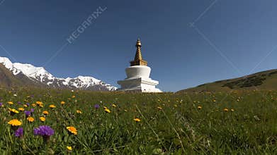White stupa standing in green meadow with snow capped mountains