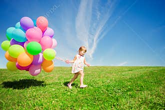 Little girl holding colorful balloons. Child playing on a green