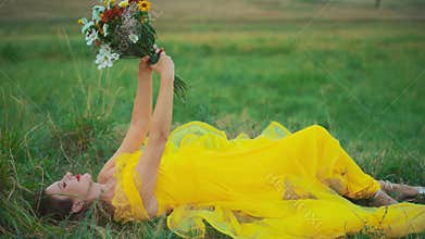 happy woman lies on green grass looking at bouquet of wildflowers, hands holding bunch of flowers daisies. freedom from