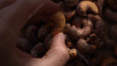 Person picking raw cashew nut from pile in sunlight