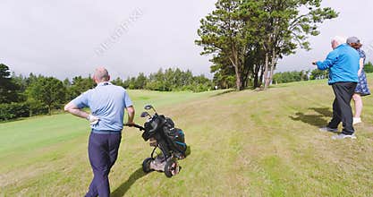 Golf players playing golf and standing with clubs and talking on golf course on cloudy day