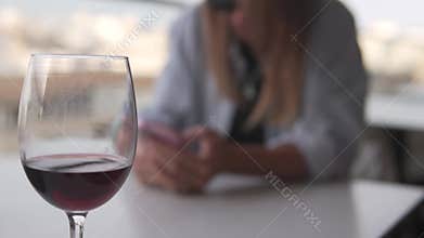 A woman drinks red wine at a table while using her phone