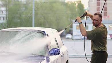 A middle aged man enthusiastically cleans his blue car.