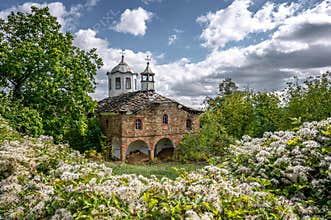 BULGARIA: Historic stone Orthodox church surrounded by green trees under cloudy sky