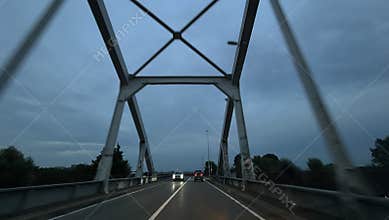 Rainy drive under steel bridge on wet highway at dusk with cars