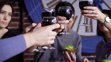 A group of cute young people in a modern restaurant at a table with snacks. Men and girls are baked with glasses of wine