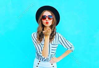 Fashion portrait pretty woman with red lips is sends an air kiss in a sunglasses shape of heart over blue