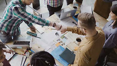 Top view of young business team working together near the table, brainstorming. Two mans fist greeting each other.