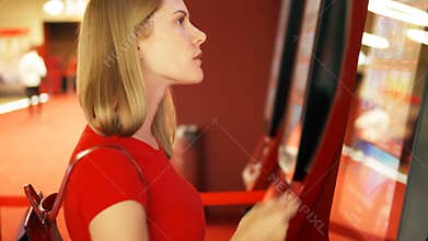 Young pretty woman in red t-shirt buying movie ticket from vending machine at cinema
