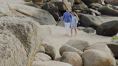 A young happy beautiful couple of lovers, in blue clothes are holding hands, walking along the seashore, smiling