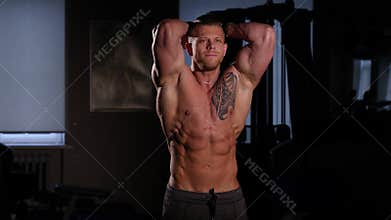 Young bodybuilder with a bare torso posing in a gym. 60 to 24fps 4K