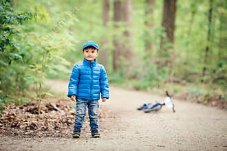 boy toddler in blue jacket, jeans and baseball cap in park playground outside with bike on spring autumn day