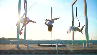 Three beautiful girl performing acrobatic stunts on the roof at sunset.