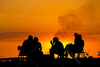 People in camping sitting near campfire against sunset