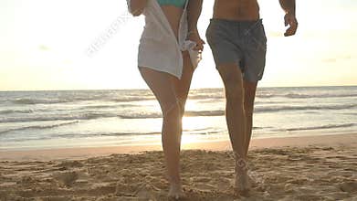 Young happy couple walking on the beach and holding hands of each other at sunset. Man and woman going on sea shore