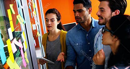 Smiling executives discussing over sticky notes on glass wall