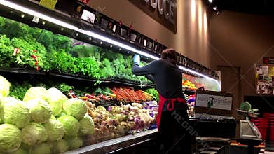 Worker exhibiting vegetables on the display rack for sale