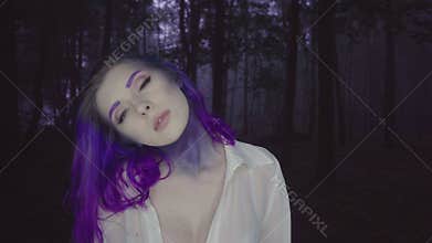 Closeup of beautiful woman in purple hair and makeup in dark forest - fairytale scene.
