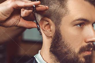 The hands of young barber making haircut to attractive man in barbershop