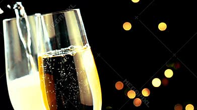Pouring champagne into flutes with golden bubbles with golden abstract blinking blurred Christmas tree lights bokeh