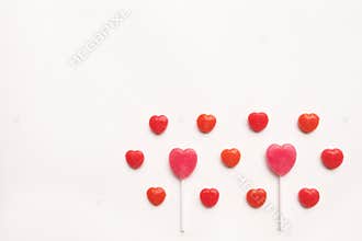 Pink Valentine`s day heart shape lollipop small red candy in cute pattern on empty white paper background. love concept. top view.