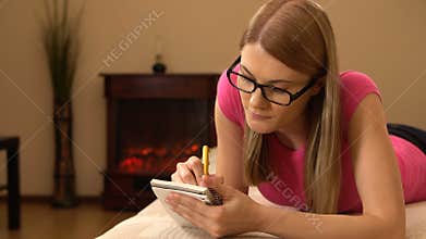 Beautiful attractive young woman writing in a notebook. Making a list, thinking and smiling. 00339