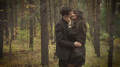 Happy couple having a date in the forest. Smiling man and woman are standing among the trees and embracing each other