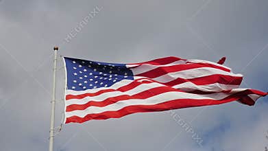 Large US flag on a background of gray sky, beautifully illuminated by the sun