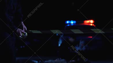 Police officer rolling tape on crime scene, protecting evidence from onlookers
