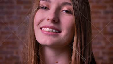 Close-up portrait of redheaded caucasian girl in braces watching into camera and smiling on bricken background