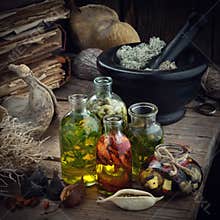 Bottles of essential oil or potion, mortar of dried moss, old books, dry roots and plants on old wooden table.