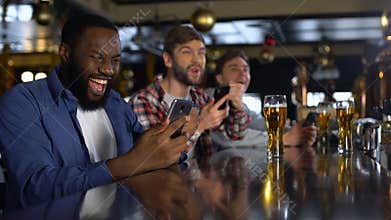 Men in bar celebrating successful bet on sports, using online bookmaker on phone