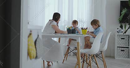 Happy family young beautiful mother and two sons draw with colored pencils sitting at the table in the kitchen. The