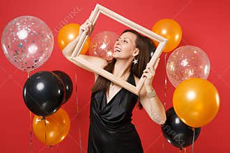 Smiling young girl in little black dress celebrating, looking up, holding picture frame on bright red background air