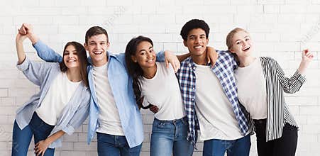 Diverse teenagers embracing and having fun over white wall