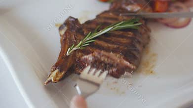 Closeup of the hand of a woman who, with the help of a knife and fork, eats roasted steak in a restaurant.