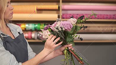 Side view of professional female floral artist arranging beautiful bouquet at flower shop. She is combining different