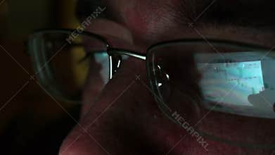 Reflection in glasses of stock market trade information from screen of tablet.
