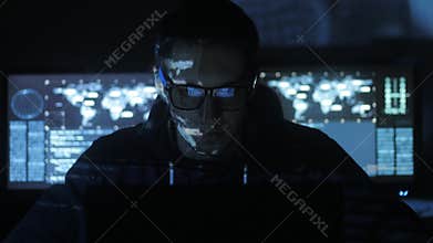 Male hacker programmer working at computer while blue code characters reflect on his face in cyber security center