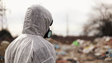 Virologist man in protective costume and respirator gas mask walking near landfill site pollution, ecological disaster