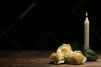 Beautiful white roses and candle on table against black background